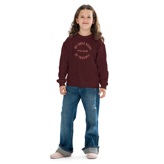 youth crew neck sweatshirt with 'My Smile Keeps Me Out of Trouble' text design